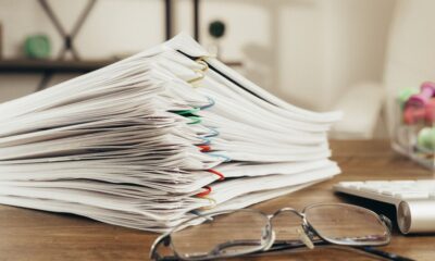 Stack of clipped company filing documents on a desk beside glasses and a keyboard