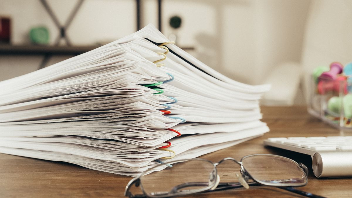 Stack of clipped company filing documents on a desk beside glasses and a keyboard