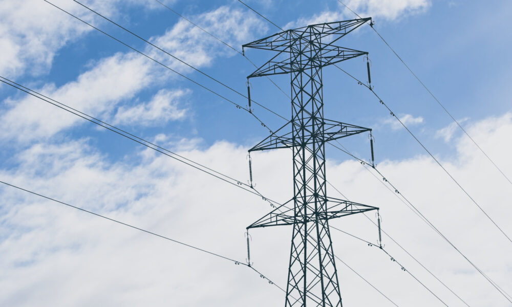 An electric tower and cables with a blue cloudy sky in the background