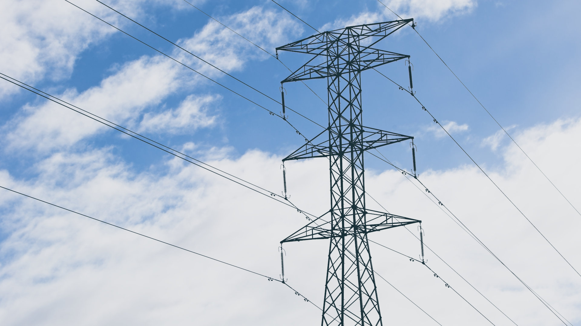 An electric tower and cables with a blue cloudy sky in the background