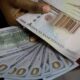 A hand holding 1000 Naira notes and 100 Dollar notes
